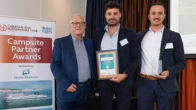 A Caravan and Motorhome Overseas Campsites Award Winner with the Chairman next to a sign showing Campsite Partner Awards, with Irish Ferries below it