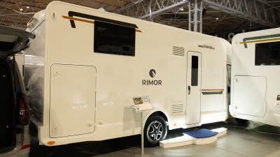 The Rimor Sarus Plus 66 has a white exterior with black and gold decals.  There is a large step outside its habitation door.  It has a large garage towards the rear.