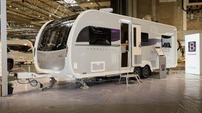 Buccaneer Aruba exterior’s grey with purple decals.  The entrance door is open and there is a fixed metal step into its interior.  There is an interactive stand towards the rear of the caravan.