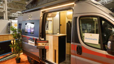 The Pilote V540G has a grey exterior with a red striped decal.  Its rising roof and sliding door are open.  There is a stand next to the open door.