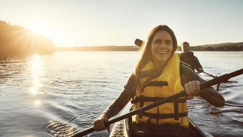 Woman paddling kayak on calm water as the sun sets