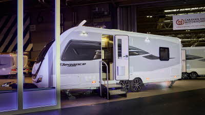 Swift Elegance Grande 850L’s exterior is white with grey sides, it has a black and bronze decal.  Its entrance door is open with two metal steps to gain easy access.  It has a roof light open.