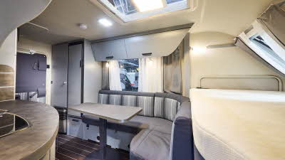 Interior of the Knaus Sport&Fun 480 QL Black selection with blue and grey striped sofas, wooden accents and a wooden floor. The fixed French transverse bed is at the front.