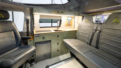 Wildtracks Campervans Explorer has a cream floor with black leather upholstery.  The cabinets are green.  The rising roof is open.
