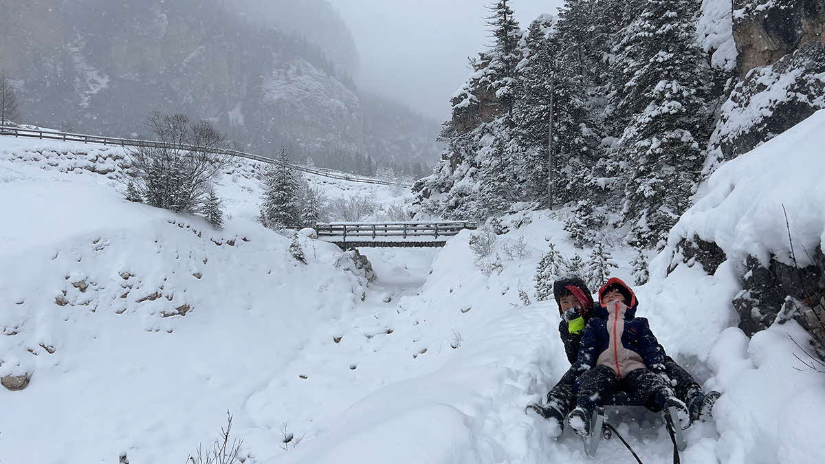 Snowy mountain scene with two children on a sledge.