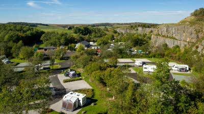 Aerial view of leafy caravan site on sunny day next to rocky cliff