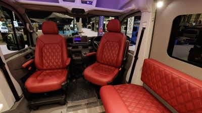 The Bespoke Leisure Bespoke Edition Volkswagen Crafter has red upholstery.  The front two seats are swivelled to face into the conversion.  The floor is pale wood and there is removable carpet in the driver's cab.
