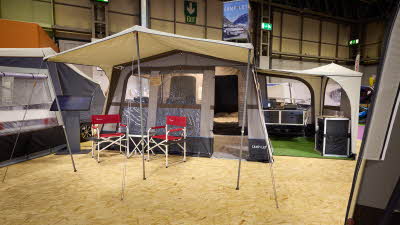 The Camp-Let Earth has a cream canvas roof with a brown canvas for the main tent.  It has a separate annex for the kitchen.  There are two red camping chairs under the canopy.  The doors are open revealing the bedroom and kitchen units.