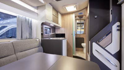 Swift Voyager 540 has grey upholstery and has a large table.  The overhead lockers are a mixture of cream and brown.  To the rear, up a step is the end washroom.  