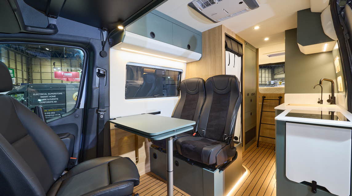 Project Yonder Freedom 4X Utility has a wooden floor with blue cabinets.  The upholstery is black and there is feature lighting under the chairs.  There is a ladder to the fixed rear bed. 
