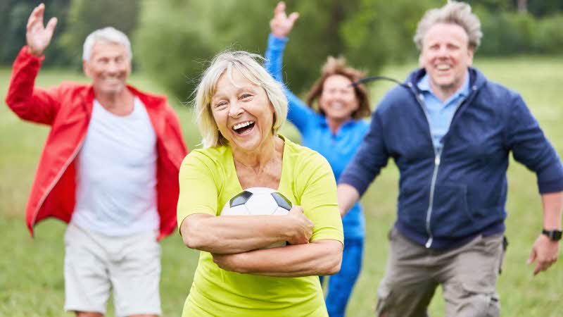 a group of adults playing a game, the woman in front hugging the football to her