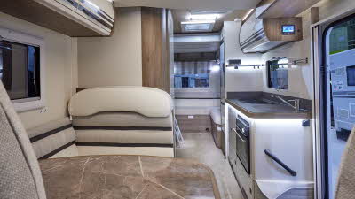 Roller Team T-Line 700 has white and brown upholstery with matching overhead lockers.  The carpet is cream.  There is a large marble effect table.  Towards the rear there is a rear lounge.  