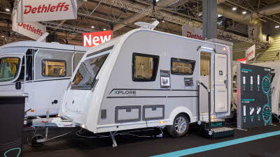 The Xplore XC LITE is white with grey sides and black decals.  There are two metal steps to gain easy access.  There is a large Xplore advertising banner next to the LITE. 