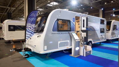 Bailey Pegasus Grande GT75 Amalfi’s exterior has grey sides with a blue and white patterned decal from the front to the rear.  The entrance door is open and there are two metal steps to gain easy access.  There is an interactive display board 