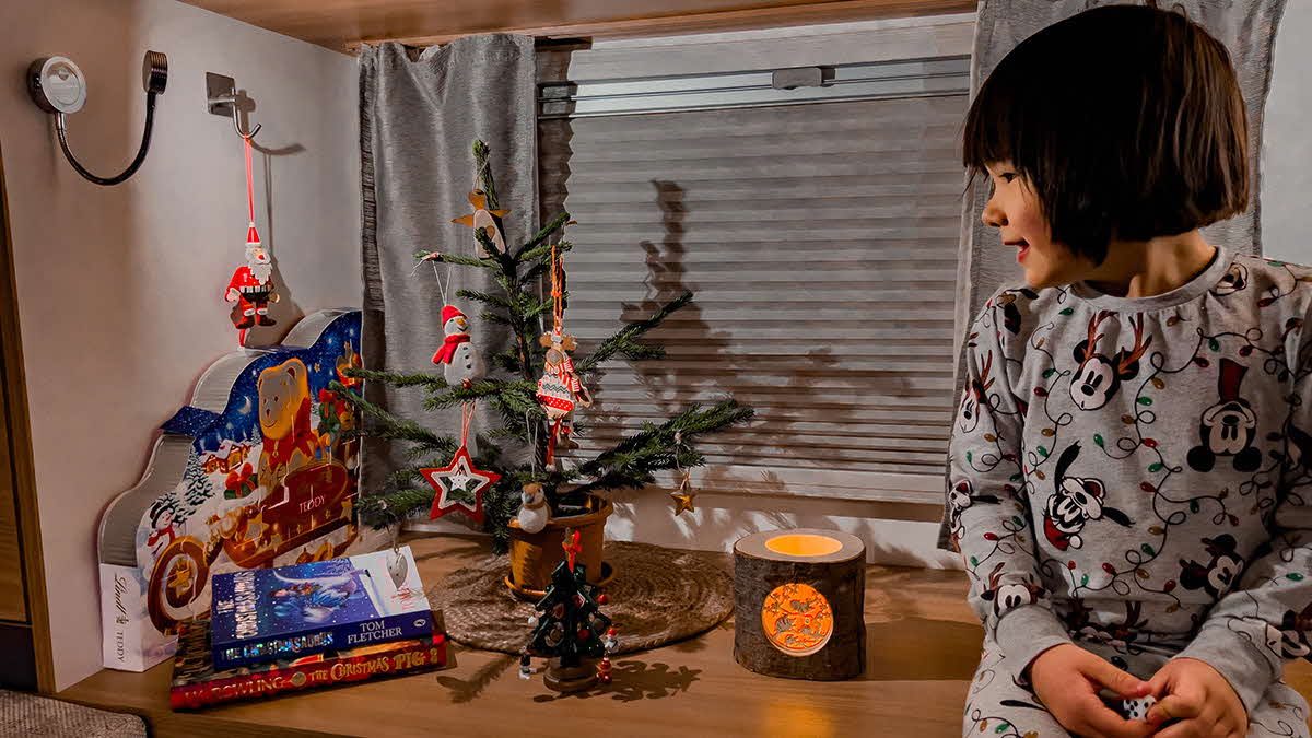 Photo of the interior of a motorhome with Marcus Leech's daughter dressed in festive pyjamas looking at a small Christmas tree.