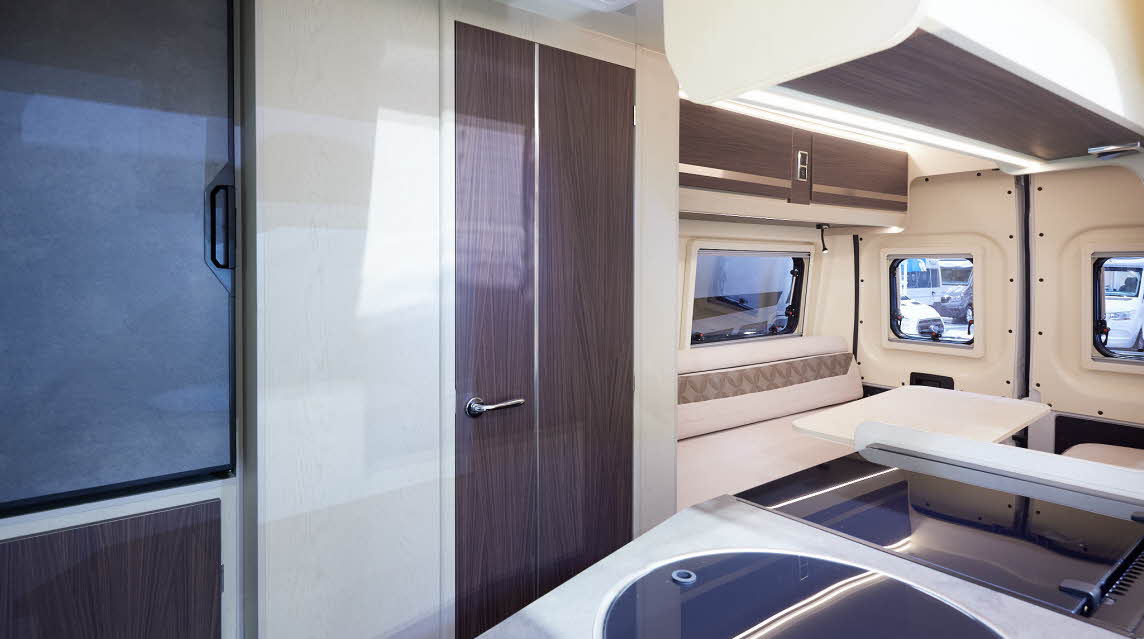 Rimor Horus 66 has two tone cream and patterned upholstery.  The doors are a dark wood.  Towards the rear is a rear lounge.