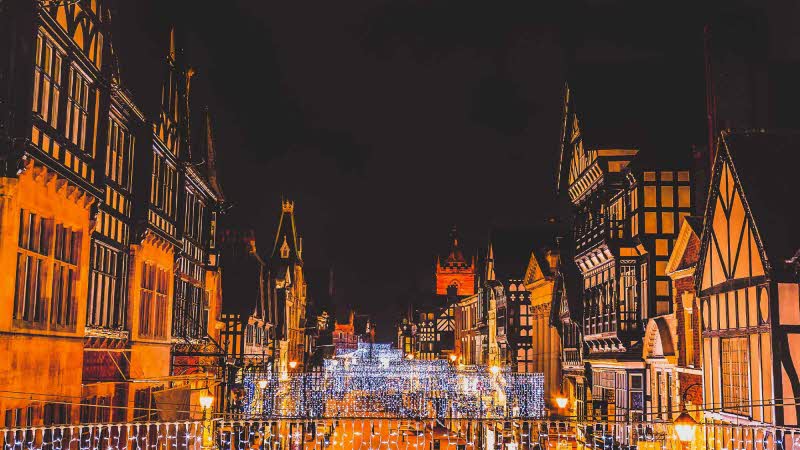 A view down the street in Chester with black and white buildings lining the street on either side with festive lights all done the street under a night sky