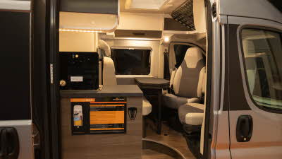 The VANTourer 540 D has brown and cream upholstery.  The front two seats are swivelled to join the dining area.  It has cream and dark wood lockers.  The floor is wooden.