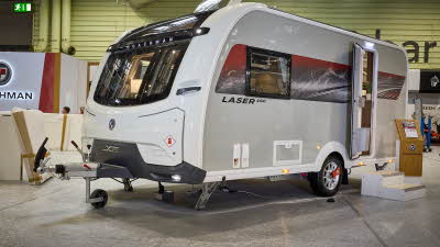The Coachman Laser 480 Xtra has a white exterior with a red and grey patterned decal.  Its sunroof is open.  The entrance door is open and there are two wooden steps to gain easy access.  There is a stand next to the steps.
