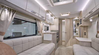 Elddis Avanté 520’s interior has cream upholstery with pale wooden furniture.  The kitchen is in the middle and the end washroom’s door is open.