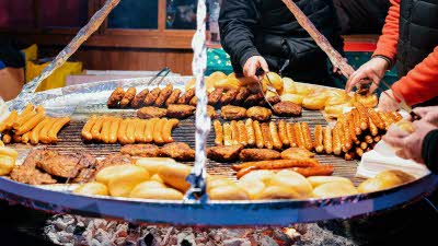 A selection of sausages and meats cooking on a hanging bbq at a Christmas market