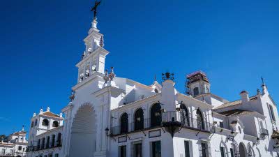 The pristine facade of the Hermitage of El Rocío gleams under the Spanish sun with its elegant white walls and ornate religious detailing standing out against the clear blue sky