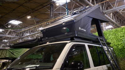 The Latitude Tents Explorer is displayed on a cream Volkswagen campervan.  It has black canvas and a hard top roof.  It has an extended platform.