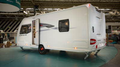 Swift Challenger Exclusive 560's exterior is white with grey and red graphics.  The caravan is a twin axle and has its corner steadies down.