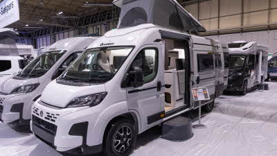 The Benimar Benivan 122 is white, its rising roof and sliding door are open.  There is a step to gain easy access