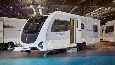 Swift Challenger Grande 640 is white with grey sides and a black front panel.  There are turquoise triangular panels at the front.  Its corner steadies are down and its entrance door is open.