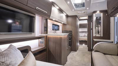 Buccaneer Barracuda interior, it is cream with dark wood furniture.  There is a L shaped sofa at the front.  The fixed bed is beyond the kitchen and there are large skylights.  