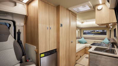 Auto-Trail V-Line 610 Sport has cream upholstery, with wooden furniture.  The floor has beige carpet.  The overhead lockers are cream.  The kitchen has a square sink and a flap to extend kitchen work surface.  The vehicle has a rear lounge.