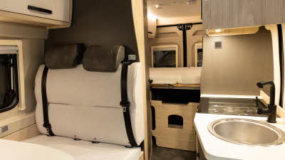 The Xplore CV X9 is has cream and brown upholstery.  The sink and hob is to the right.  The fixed bed is to the rear and the rear doors are closed.