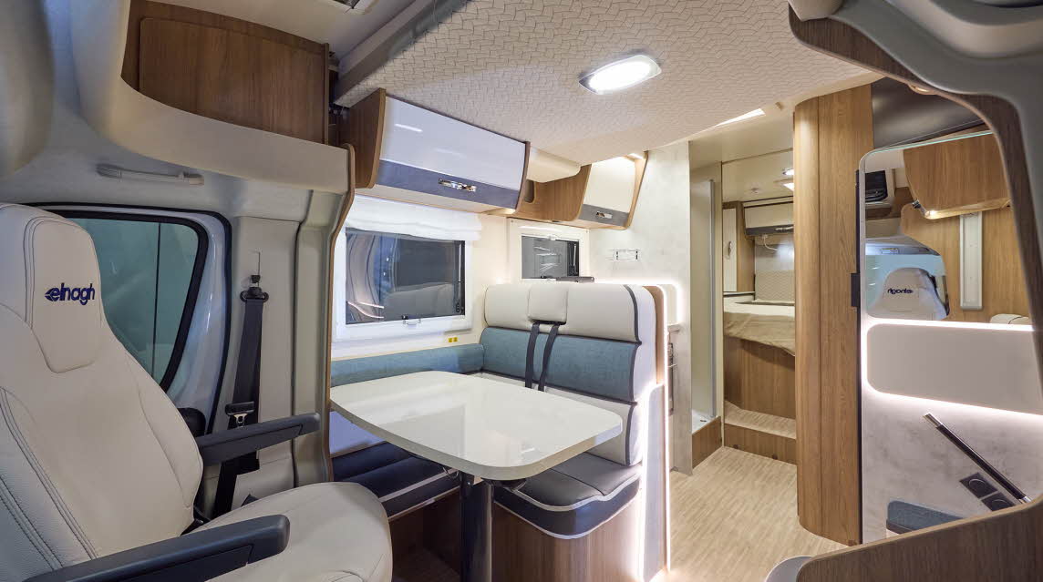 The Elnagh Baron 579 has a wooden floor and white and grey cabinets.  The upholstery is cream with grey seating and blue backrest.  There is a step to the rear fixed bed.