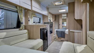 Xplore 554's interior has wooden furniture and has cream sofas with black piping.  There is a central kitchen and the bedroom is just beyond.  The rear washroom's door is open.