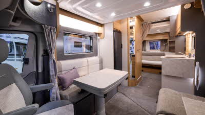 Bailey Adamo 75-4DL’s interior has beige and cream upholstery with a purple cushion.  The furniture is wooden.  The two dropdown beds are folded away and there is a beige privacy curtain tied up before the rear lounge.  