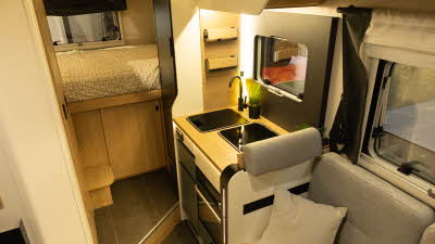 The Pilote Atlas A630G has light grey upholstery, the kitchen is in the centre and it has a rear fixed bed.  There is a wooden step for access to the bed.