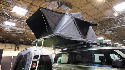 The Roof Space 4 is fully extended on a Land Rover Defender.  The canvas is pale grey, with a black porch.  There is a platform with a sturdy ladder to gain easy access.