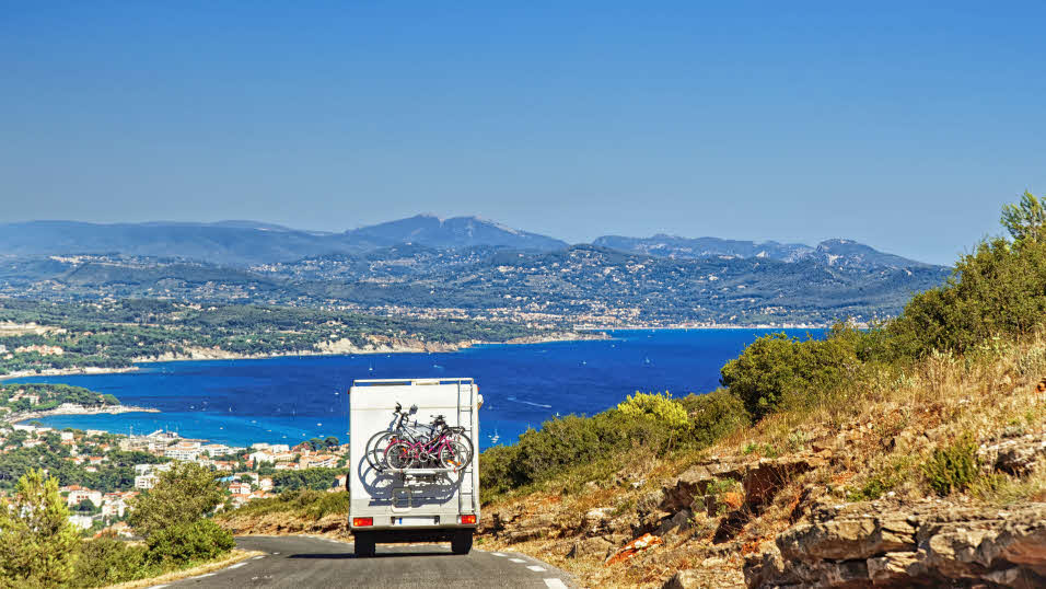 Caravan driving down the road of a mountain with a coastline view ahead