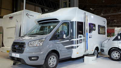 Auto-Trail F-Line F68 exterior, the motorhome has a grey cab with a white body, the habitation door is open showing into the interior, with a step to gain easy access.  There is a blue Auto-Trail umbrella in the door.