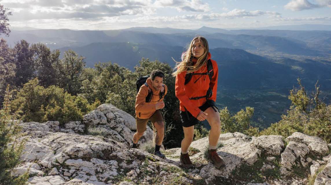 Man and woman wearing outdoor clothing walking uphill with view 