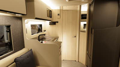 The Auto-Trail F-Line F67 has cream leather upholstery with pale wooden furniture and fittings.  The kitchen is on the left and there is an extractor fan on the ceiling.  The floor has a grey carpet.