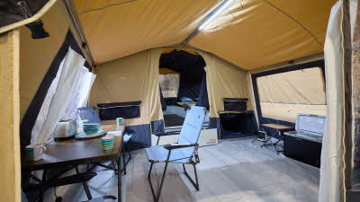 The Trigano Galleon Standard has yellow canvas, there is a cream groundsheet. There is a step to the bedroom area, there is a dining table and three blue chairs.