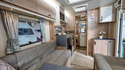 Swift Sprite Major 4 EB's interior has wooden furniture with beige upholstery and carpet.  It has dark grey work surface and table top. The bedroom is to the rear.  The skylight is open.