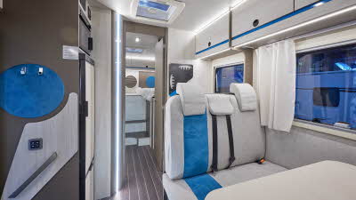 Rimor Kilig 695 has a cream interior with dark wooden doors.  There are blue accents in the upholstery, overhead lockers and décor. 
