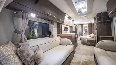 Buccaneer Cruiser interior, it is cream with dark wood furniture.  The kitchen has a full oven and an a full size fridge freezer is opposite.  The fixed bed is just beyond and there’s a rear washroom with its door open.  