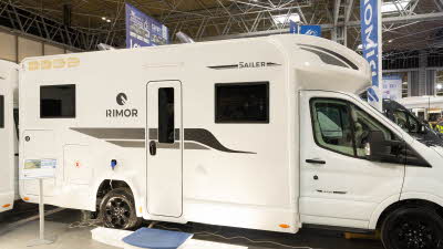 The Rimor Sailer Plus 56 has a white exterior, decorated with black and grey decals.  There is a large step outside the habitation door with a small stand to the left.