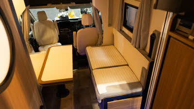 The Rimor Sailer Plus 56 has cream and beige upholstery.  There is an extendable table in front of the sofas which is shown as folded. 
